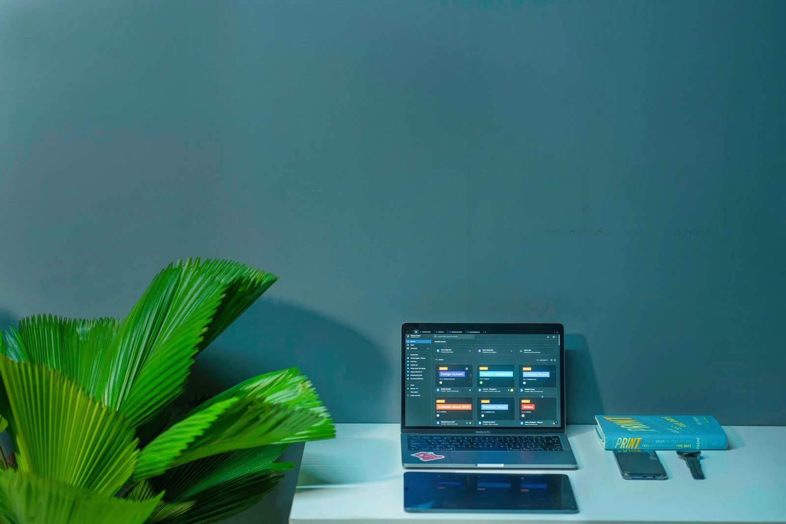 Sleek office desk setup featuring a laptop, tropical plant, and book in a modern design.